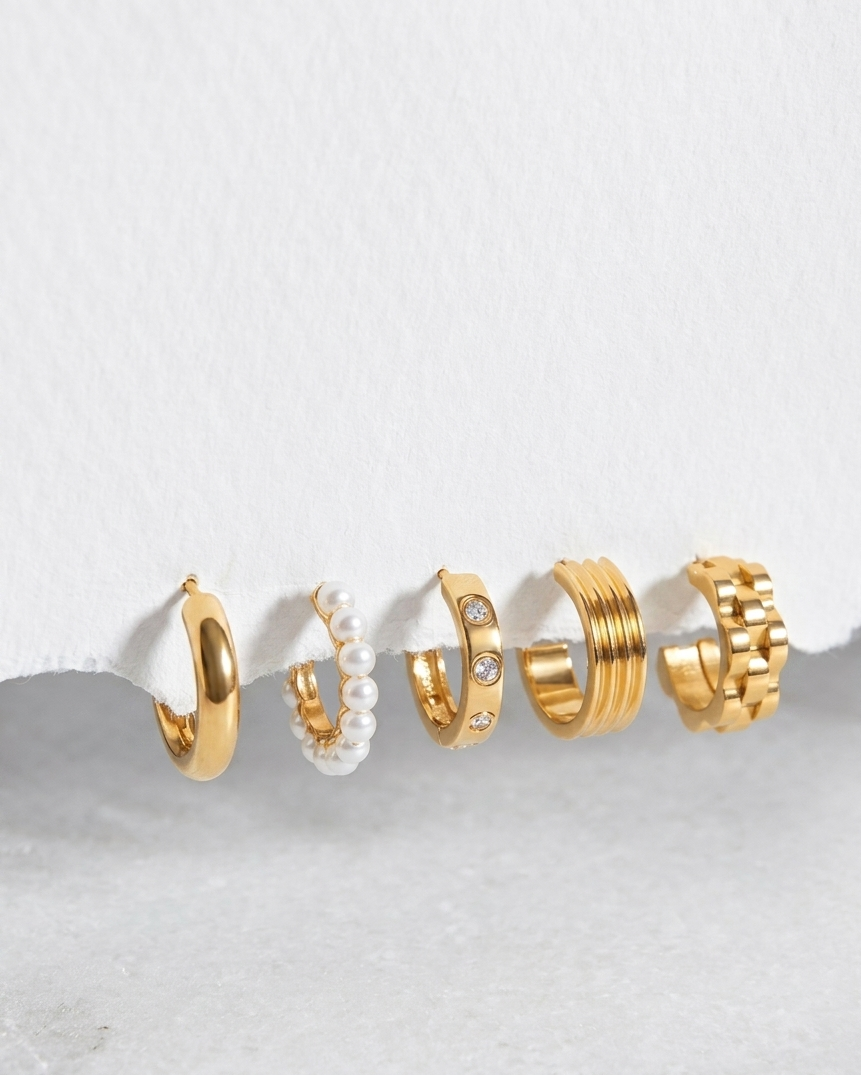 Five pairs of gold and pearl hoop earrings displayed in a row against a textured white background.
